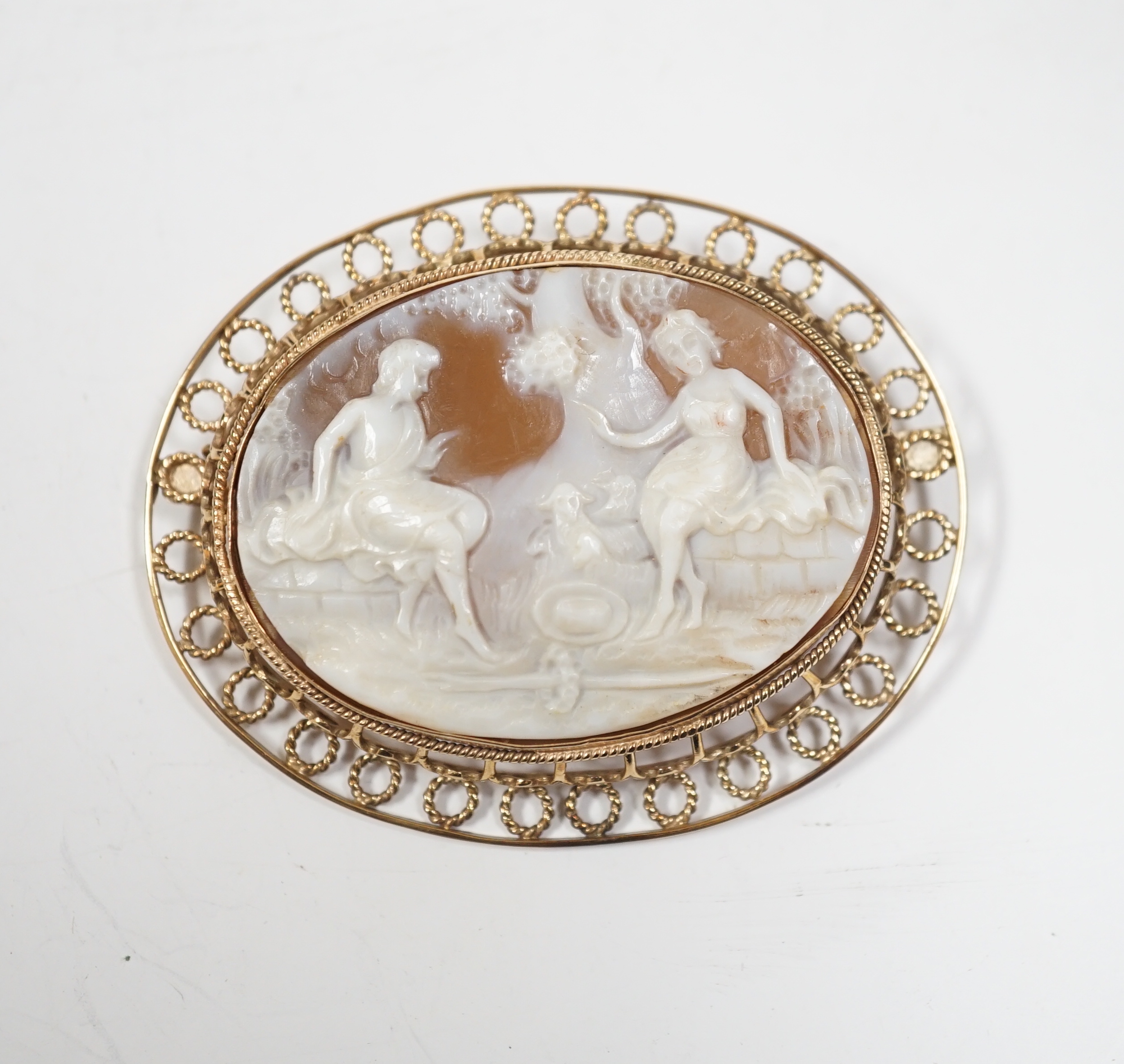 A yellow metal mounted oval cameo shell brooch, carved with two seated ladies with sheep, beneath a tree, 61mm, gross weight 19.9 grams.